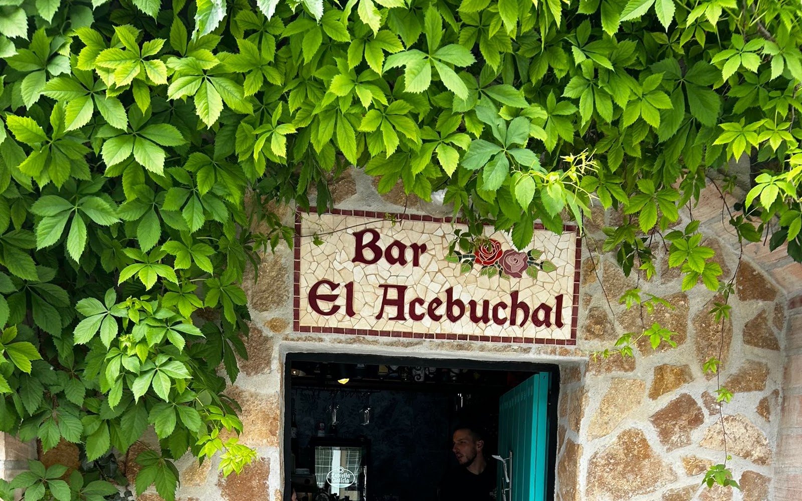 Fachada de piedra del Restaurante El Acebuchal con su placa pintada en la aldea